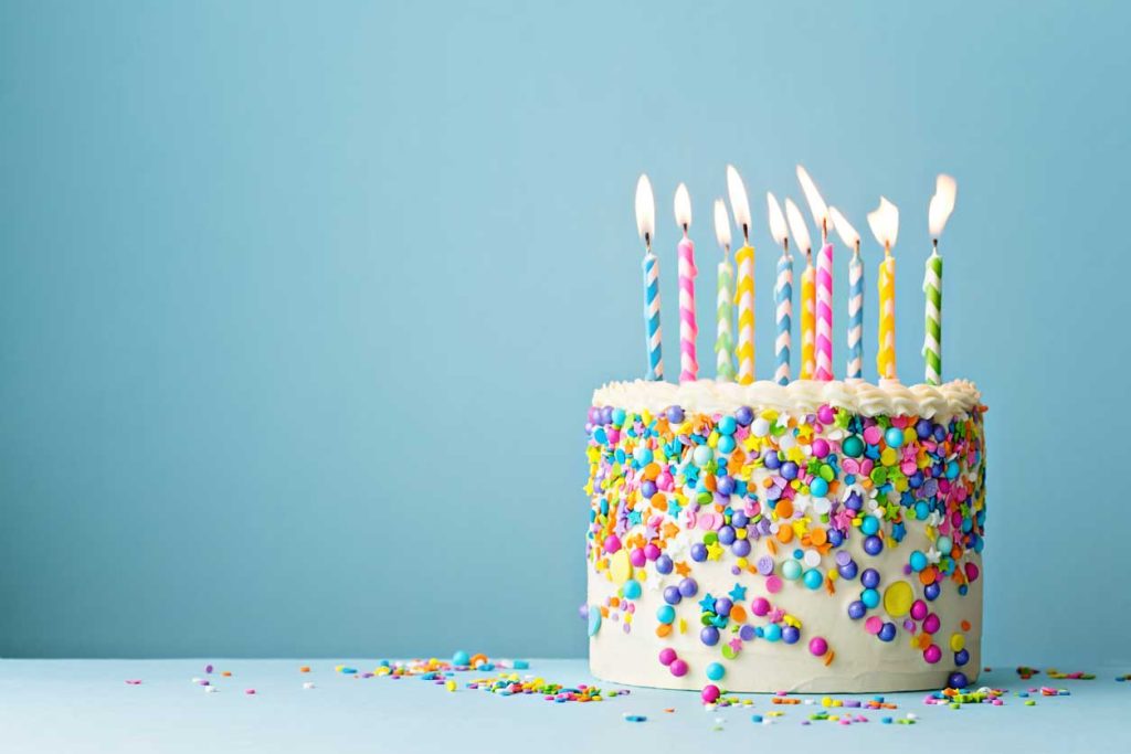 Birthday cake covered in confectionary against a blue wall.